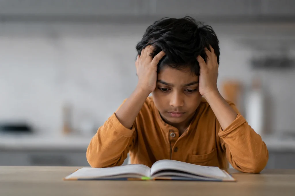 Indian child looking frustrated while studying, illustrating how learning to cope with challenges helps build resilience, confidence, and emotional strength.